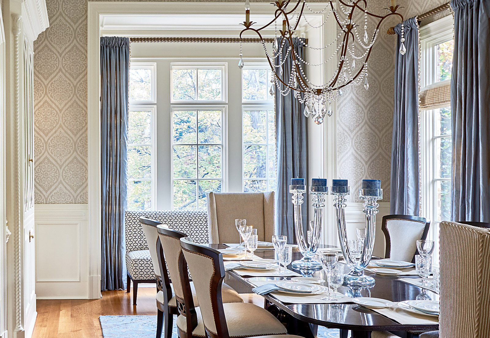 Beautiful interior design in formal dining room with crystal chandelier, beige seating and blue curtains